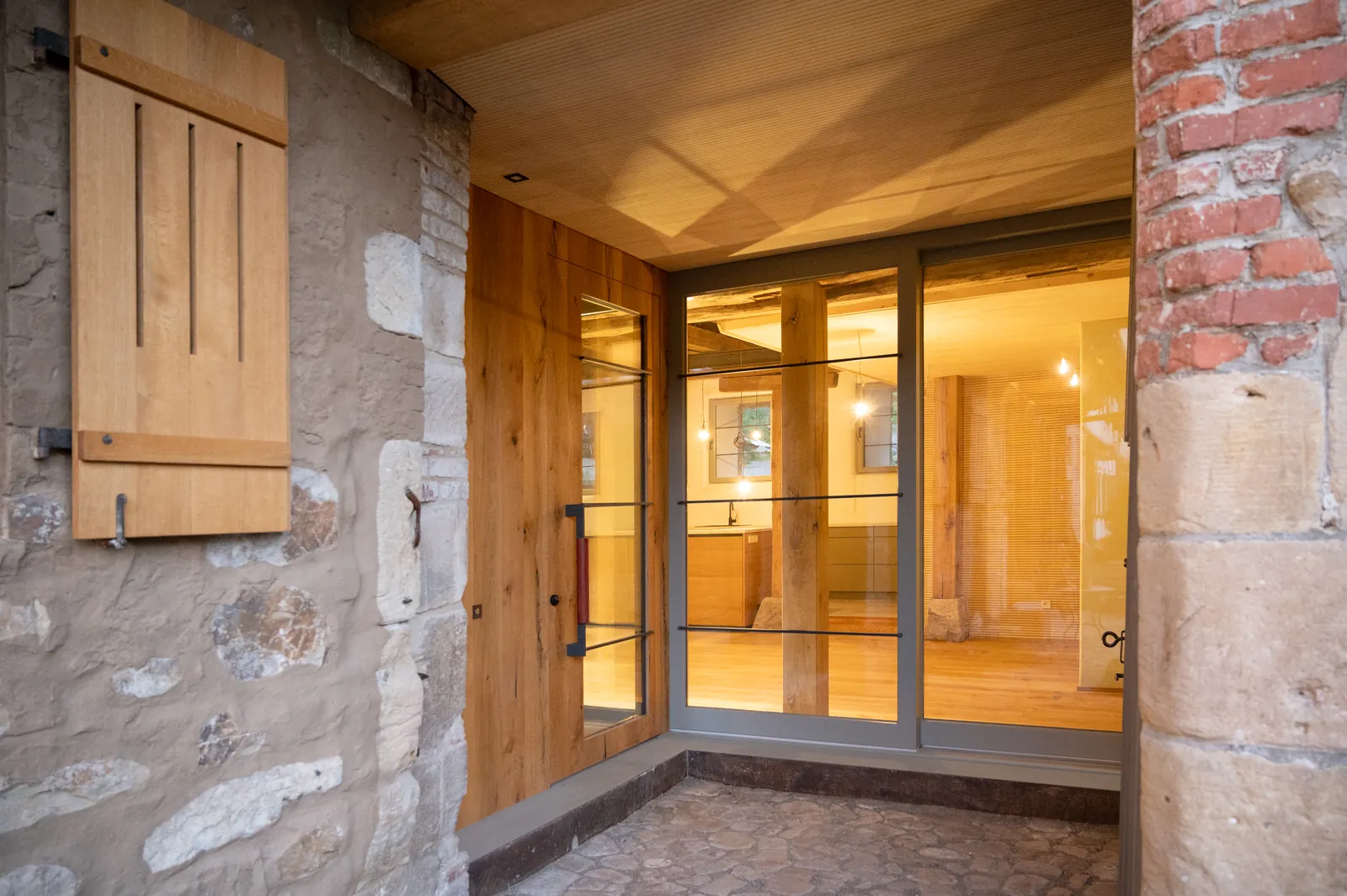 Neuer verglaster Eingang, eingefasst von altem Sandsteinmauerwerk
